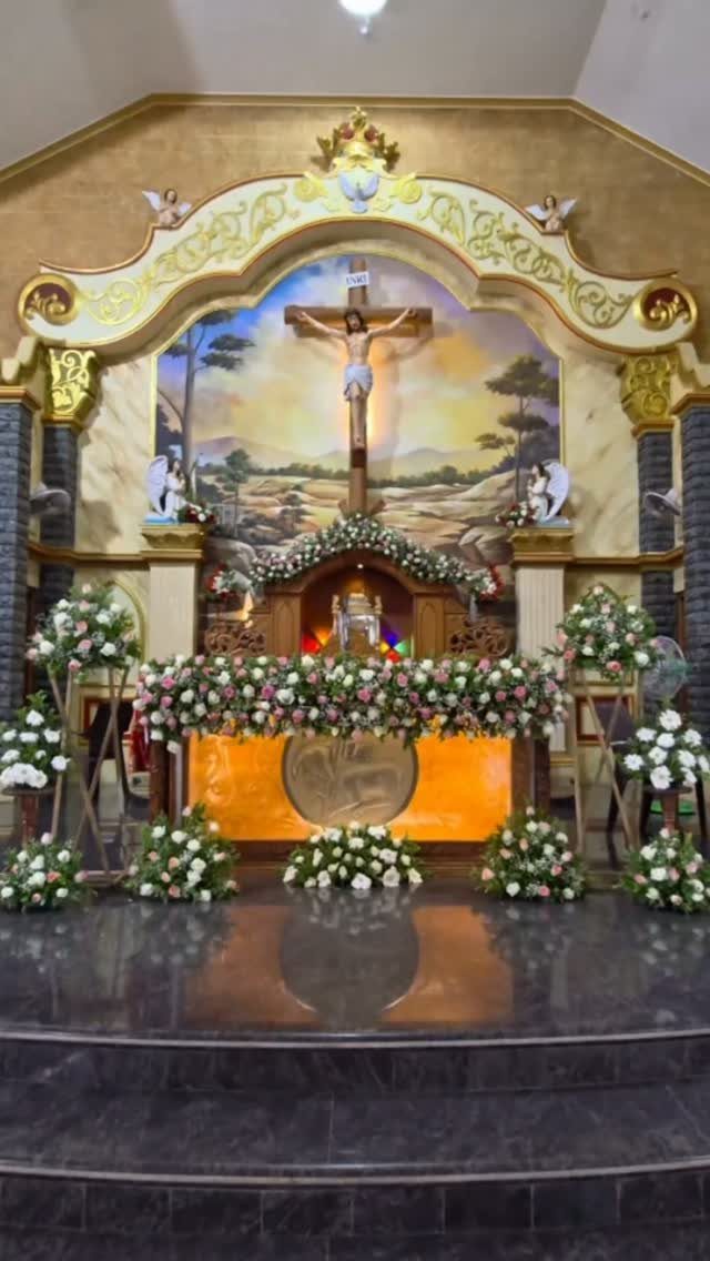 Church altar decorated with white and pink floral arrangements and a large crucifix in the background.