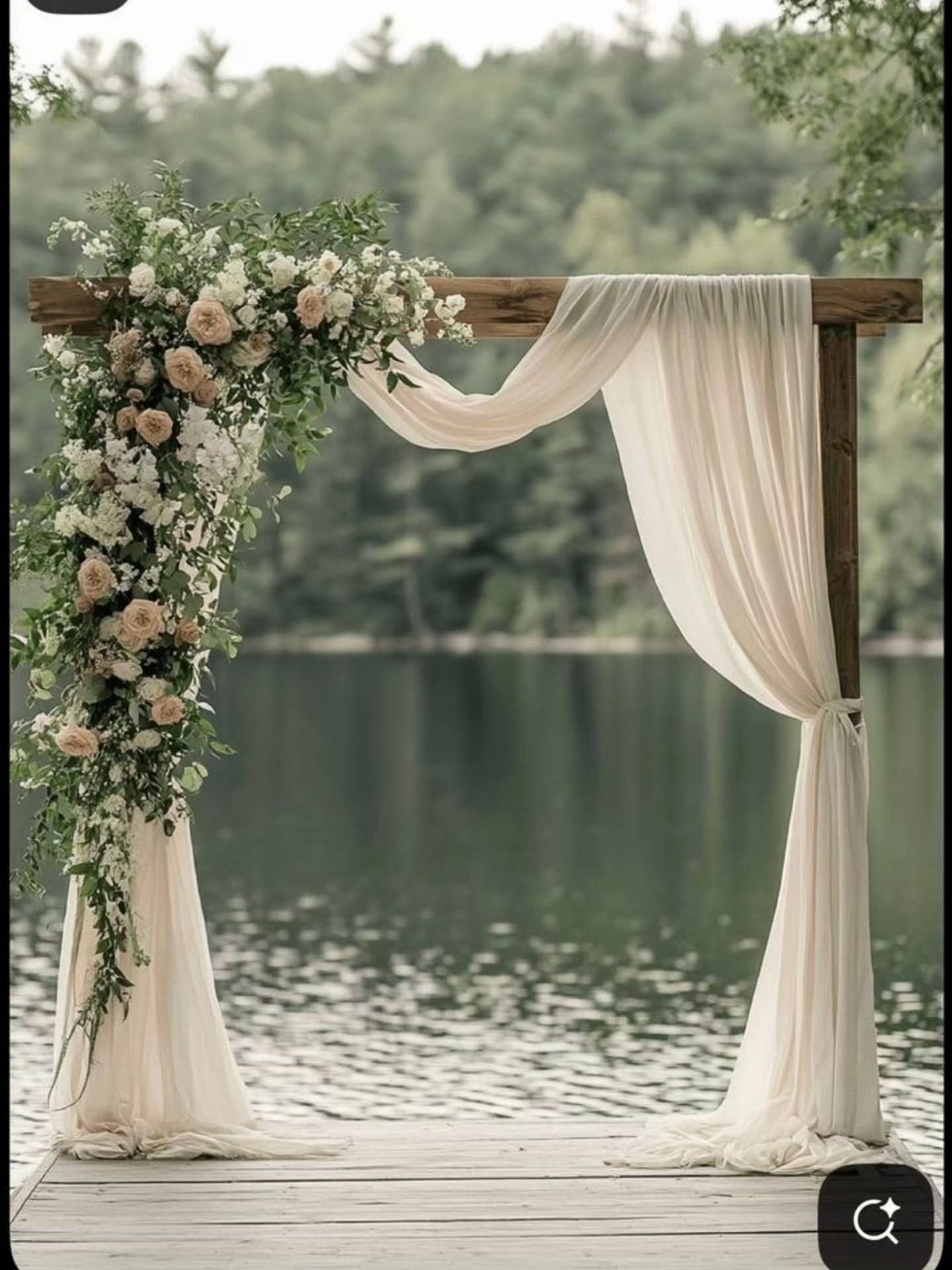 Wooden wedding arch with cream fabric and peach roses on a lakeside dock.