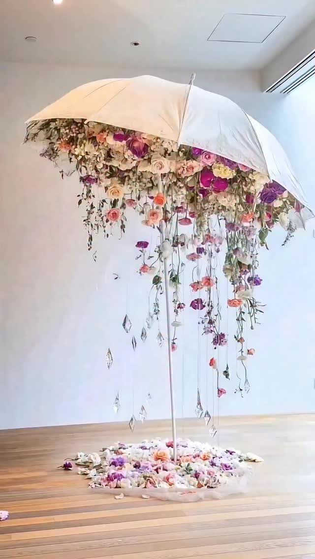 A white umbrella adorned with cascading pink and purple flowers hanging over flower petals.