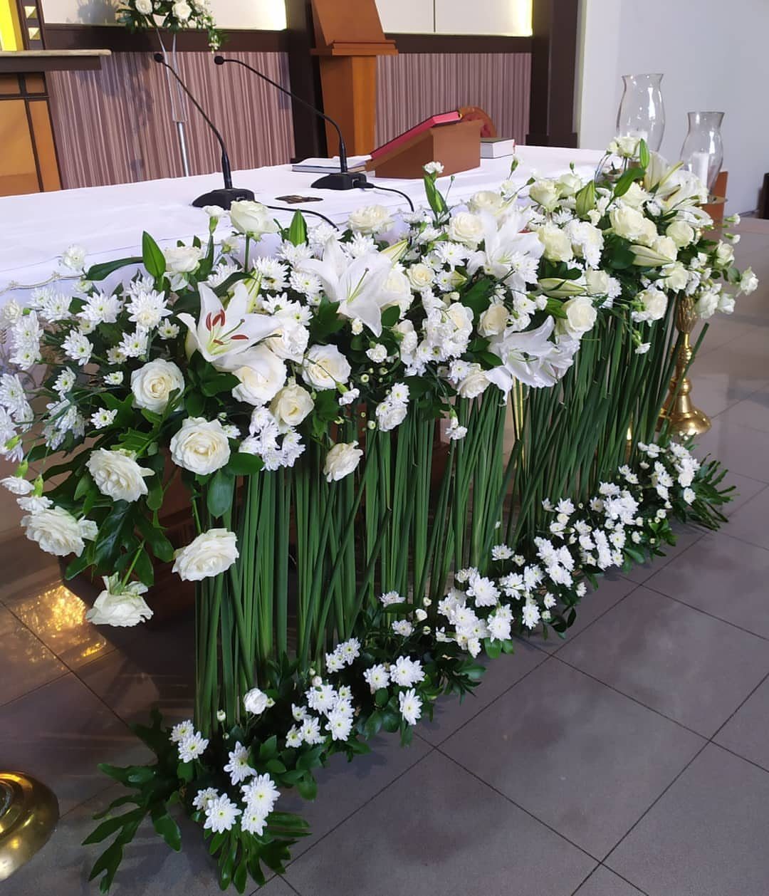 White lilies and roses arranged with long green stems along a decorated wedding table.