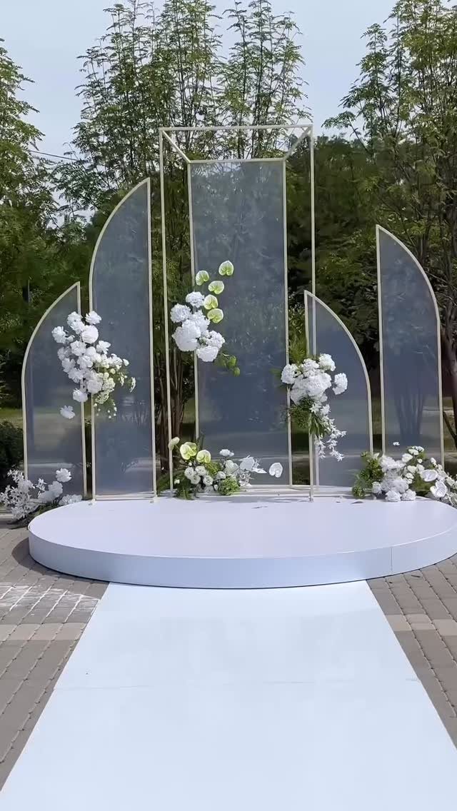 Modern wedding altar with gold-framed translucent panels and white floral arrangements on a circular platform.