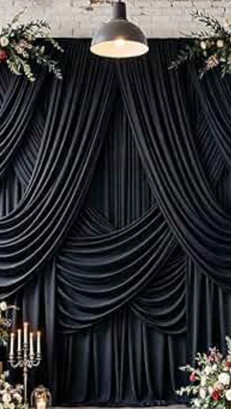Black draped fabric backdrop decorated with white floral arrangements and a hanging pendant light.