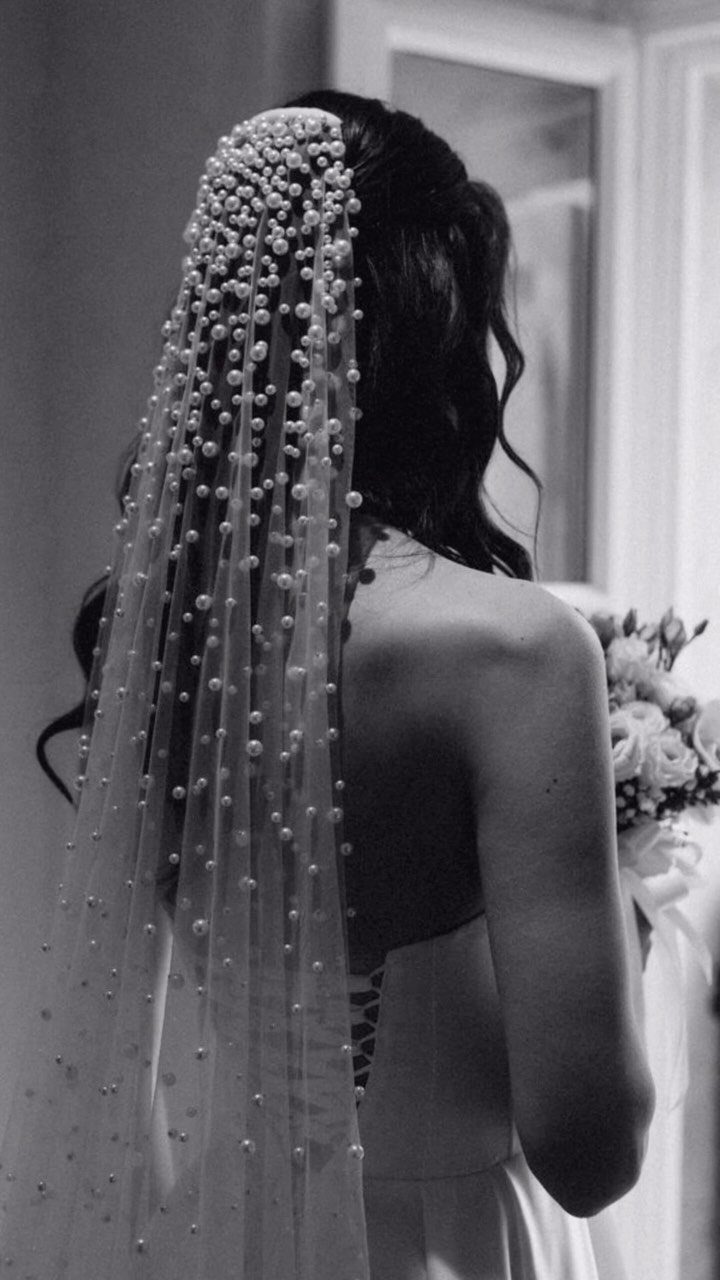 A woman wearing a long sheer veil decorated with many small pearls.