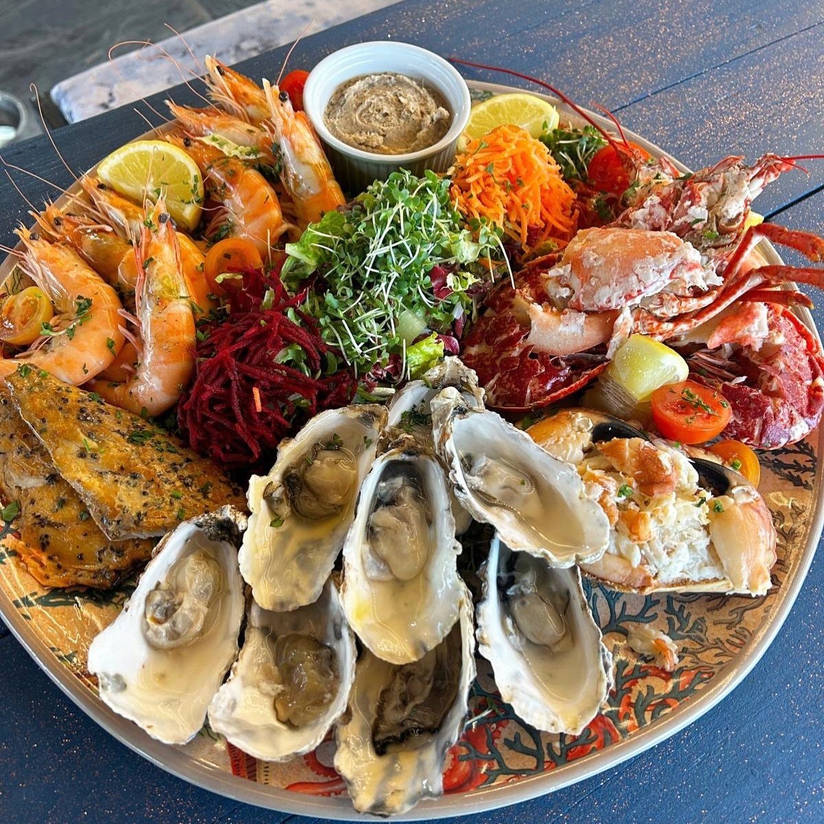 A large seafood platter featuring lobster, oysters, prawns, and grilled fish with fresh garnishes.