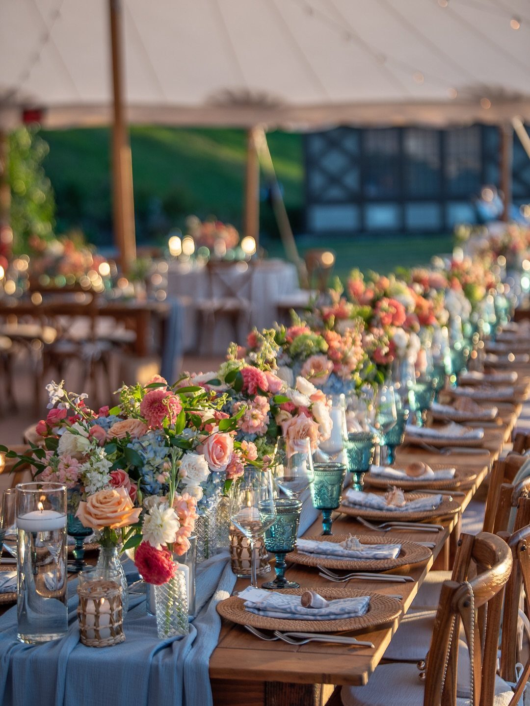 Floral arrangements in soft pink and peach tones decorate a long table with blue linens.