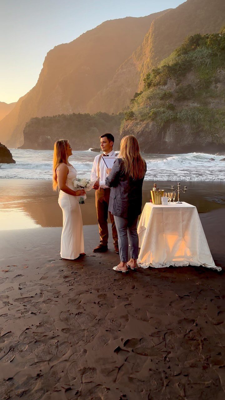 A bride and groom exchange vows on a beach during a golden sunset.