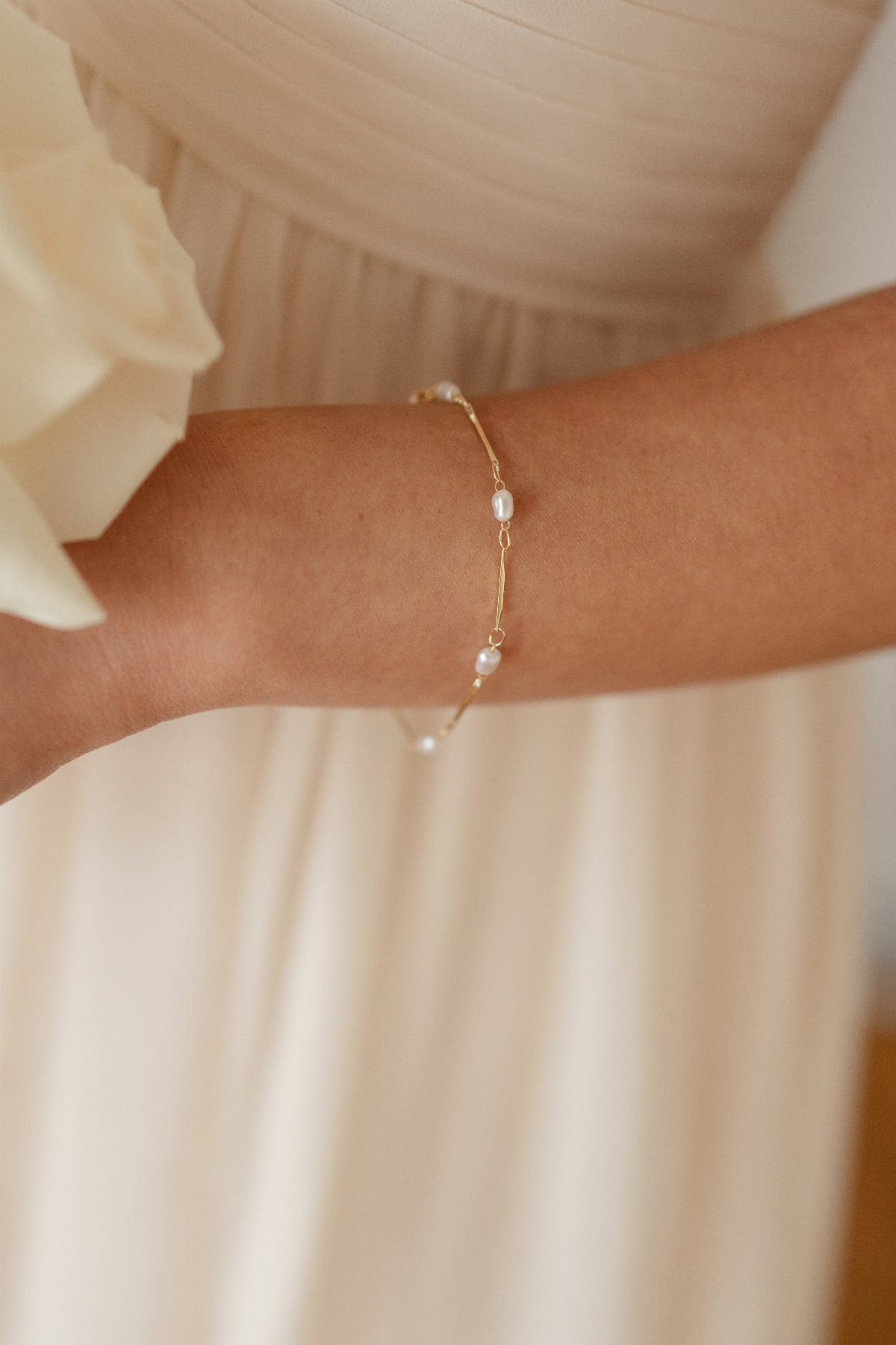 A delicate gold bracelet with small white pearls worn on a person's wrist.