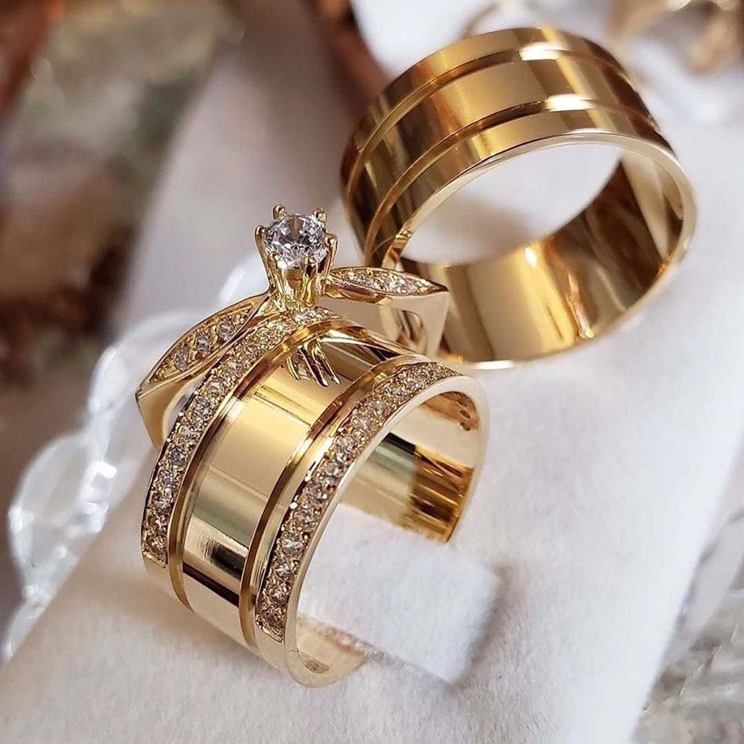 Two wide polished yellow gold rings with sparkling stones resting on a white surface.