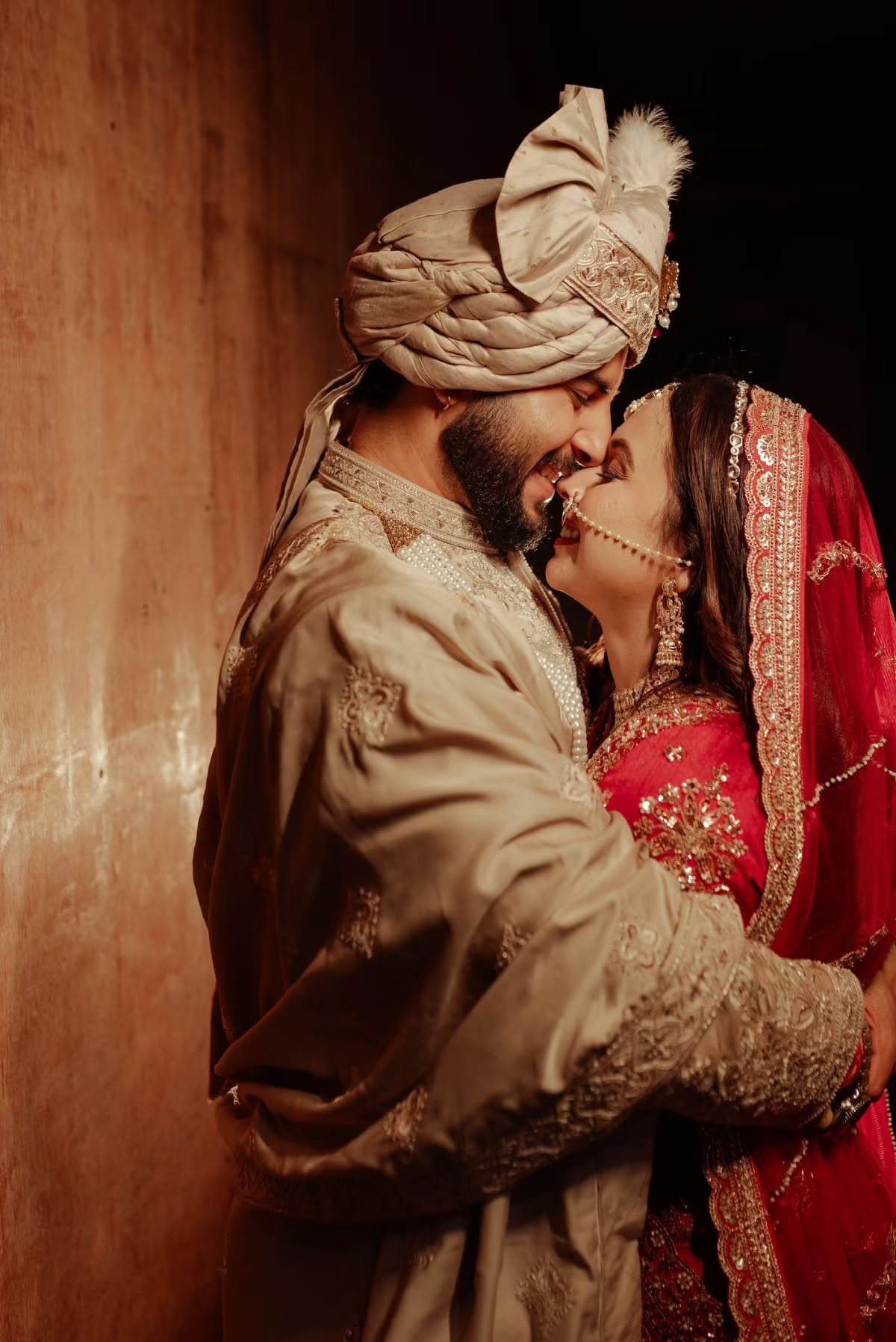 A smiling bride and groom in traditional South Asian wedding attire sharing an intimate moment.