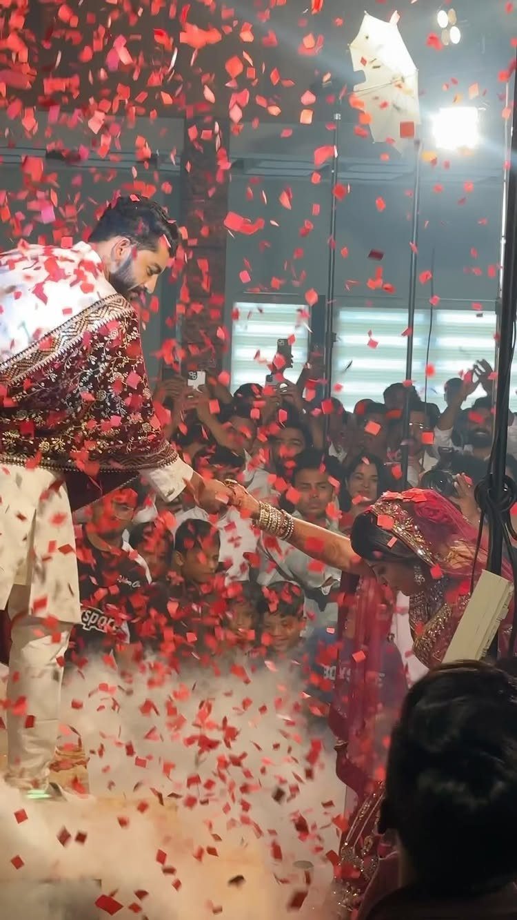 A bride and groom hold hands under a heavy shower of red confetti during their wedding celebration.