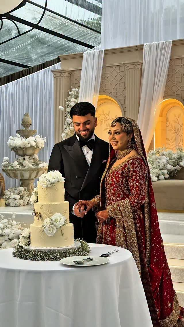 A bride and groom smiling while preparing to cut a white tiered wedding cake together.