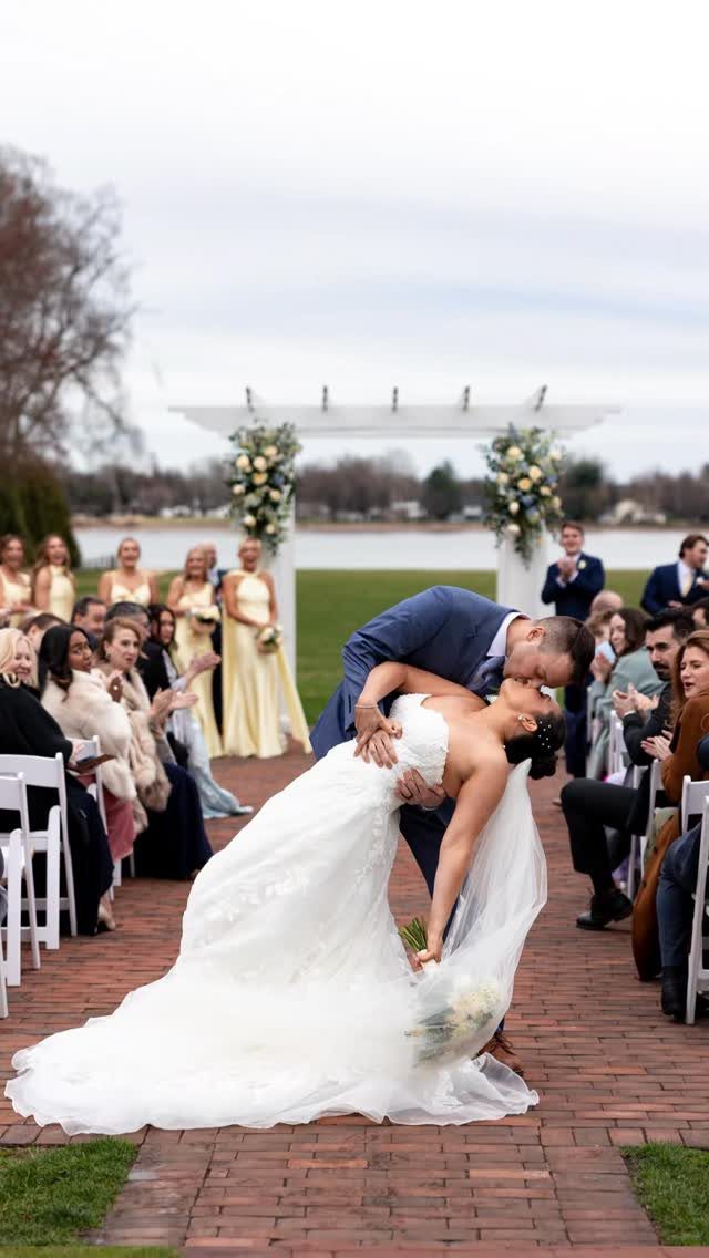 A groom in a blue suit dips his bride in a white lace gown for a kiss.