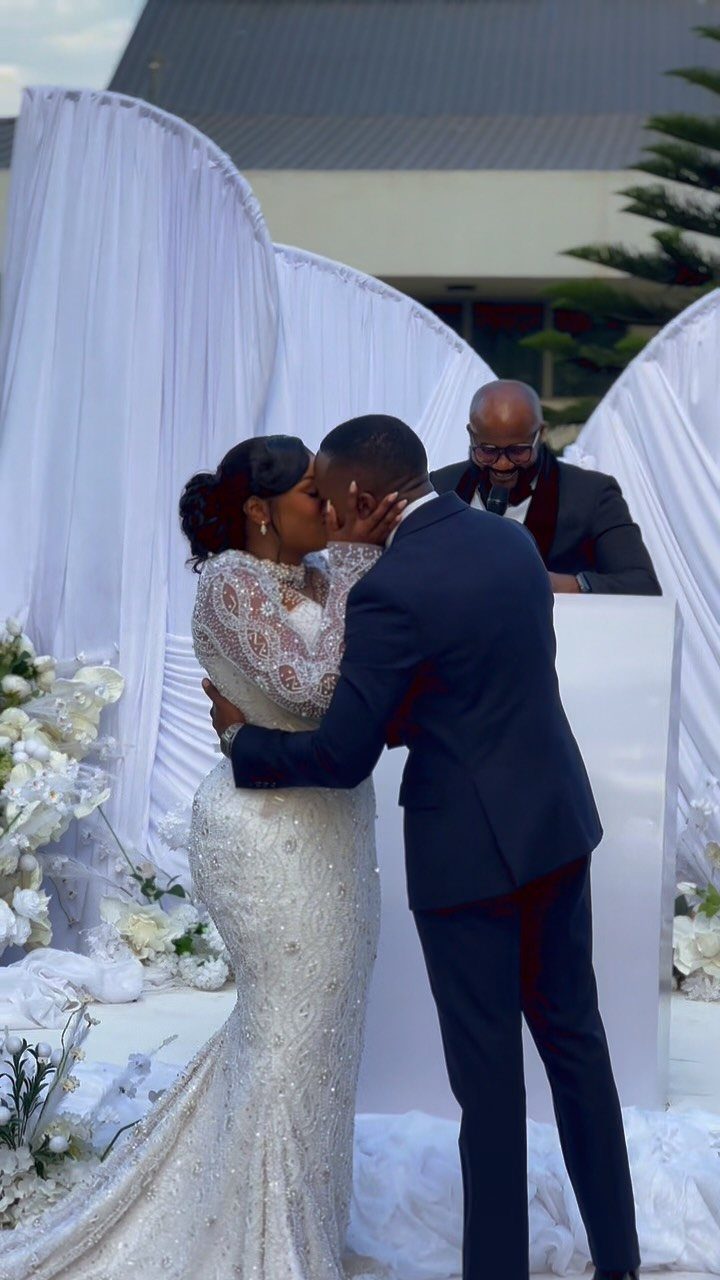 A bride and groom kissing during their wedding ceremony in front of white drapery.