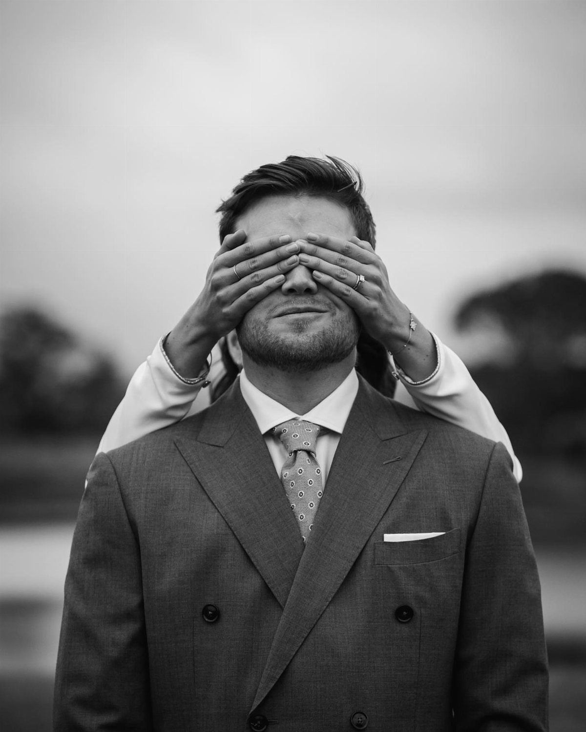 A woman's hands covering a man's eyes in a black and white portrait.
