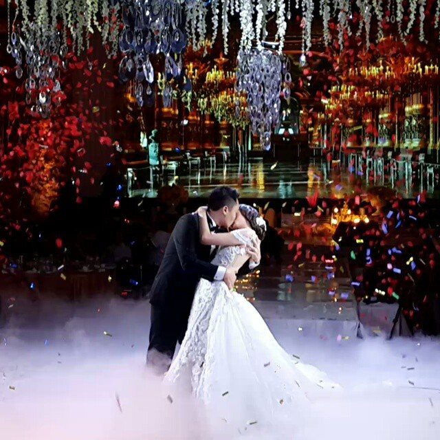 Bride and groom kissing amidst fog and confetti on a decorated dance floor.
