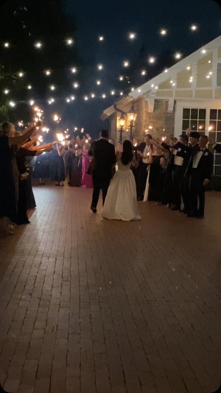 Bride and groom walking through a sparkler send-off lined by wedding guests at night.