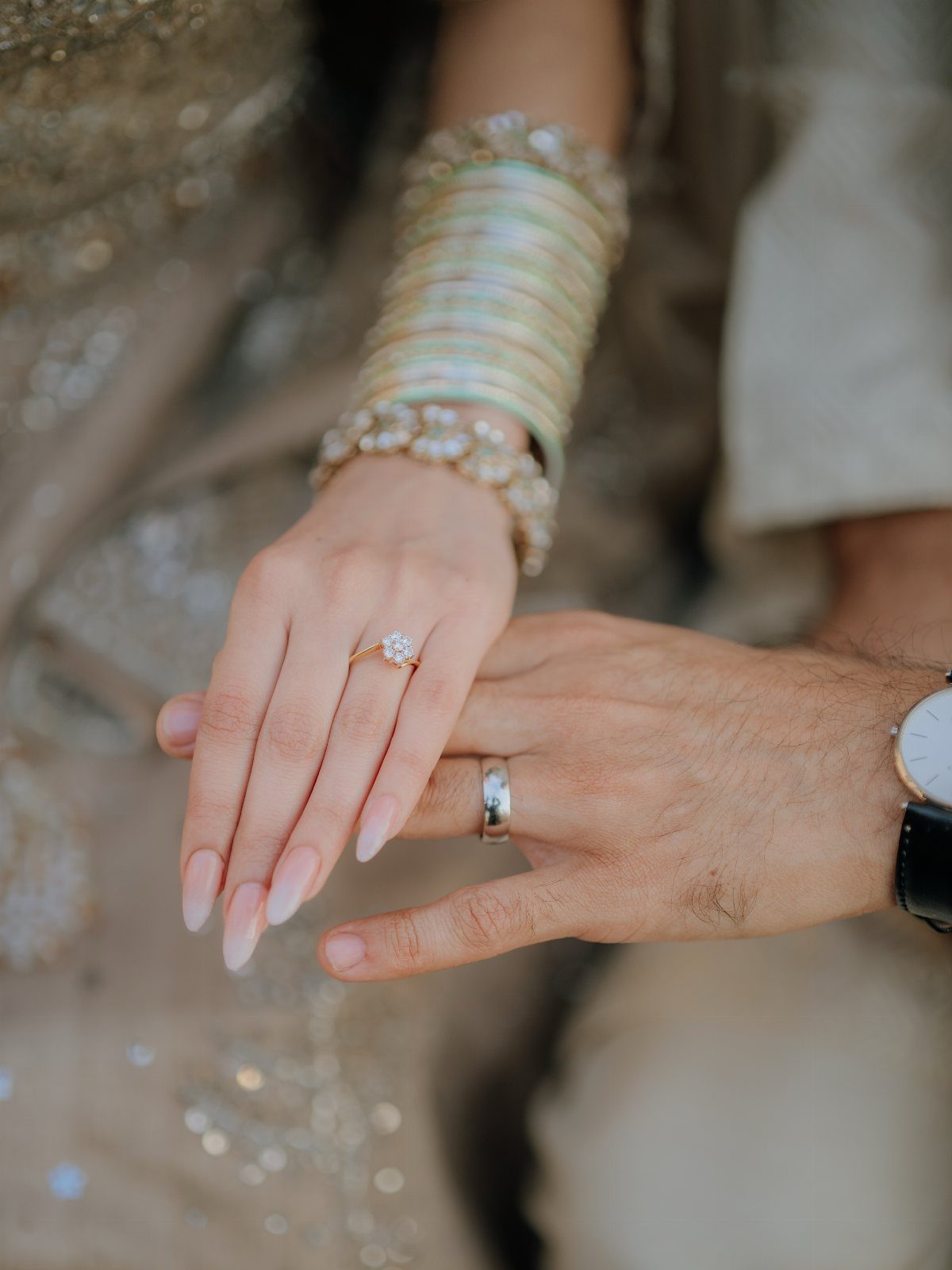 Close-up of a bride and groom's hands showing their wedding rings and jewelry.