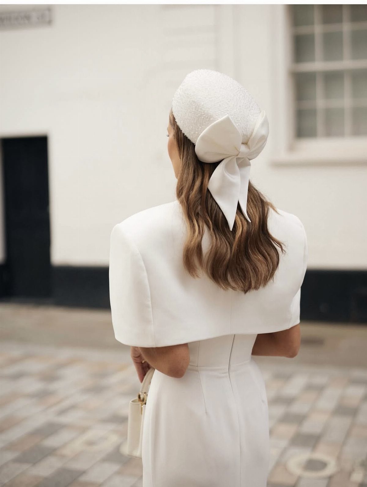 8 Civil Wedding Outfit Ideas for Brides Who Want Something Different 8 Woman in a white wedding dress and jacket wearing a white pillbox hat with a large bow.