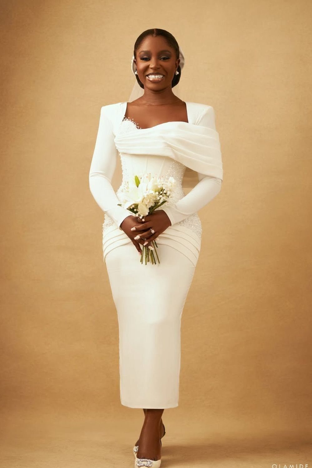 8 Civil Wedding Outfit Ideas for Brides Who Want Something Different 4 A smiling woman in a white long-sleeved draped midi dress holding a white flower bouquet.