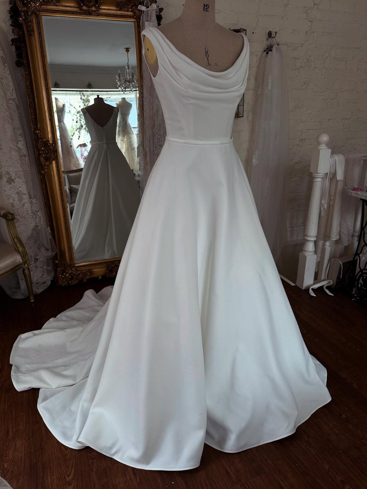 Classy Wedding Dress: 7 Styles That Photograph Beautifully 5 White satin wedding gown with a draped cowl neckline displayed on a mannequin.