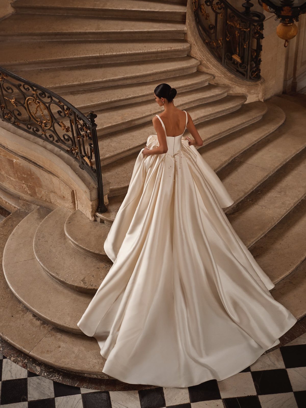 Classy Wedding Dress: 7 Styles That Photograph Beautifully 6 Woman in a voluminous white satin wedding gown standing on a curved stone staircase.