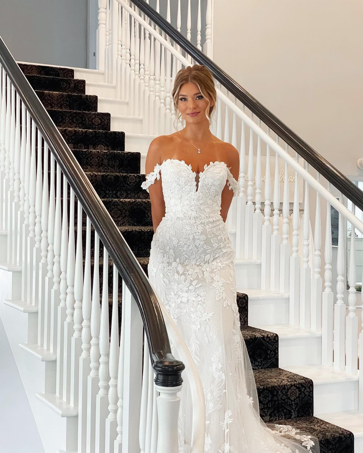 Classy Wedding Dress: 7 Styles That Photograph Beautifully 2 Woman in a white off-the-shoulder lace wedding gown posing on a staircase.
