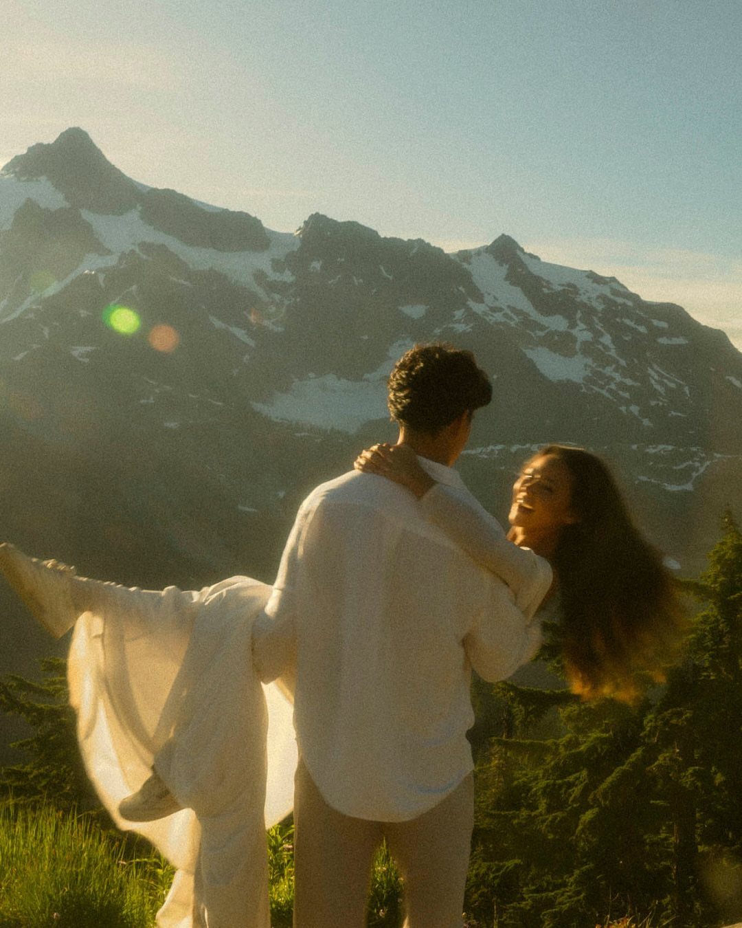 17 Couple Pictures for Your Wedding That Feel Real, Not Posed 10 A man lifting a woman in white clothing against a backdrop of snowy mountains.