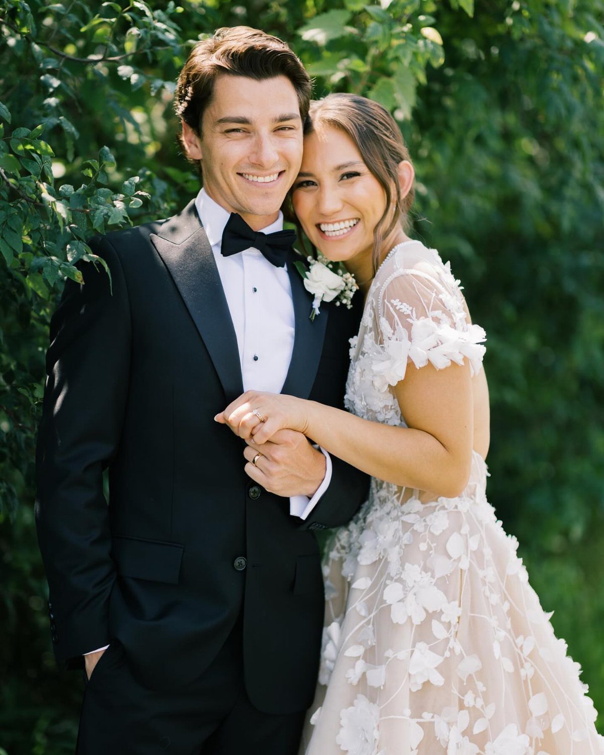 17 Couple Pictures for Your Wedding That Feel Real, Not Posed 11 A smiling bride and groom posing closely together against a backdrop of green leaves.