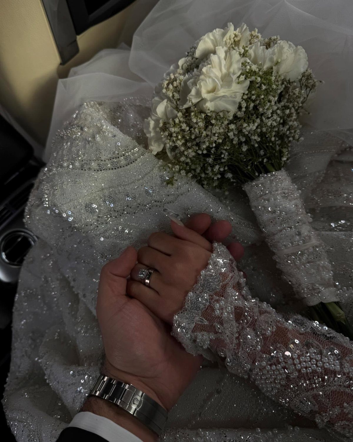 17 Couple Pictures for Your Wedding That Feel Real, Not Posed 3 A couple holding hands over a white sequined wedding dress and a rose bouquet.