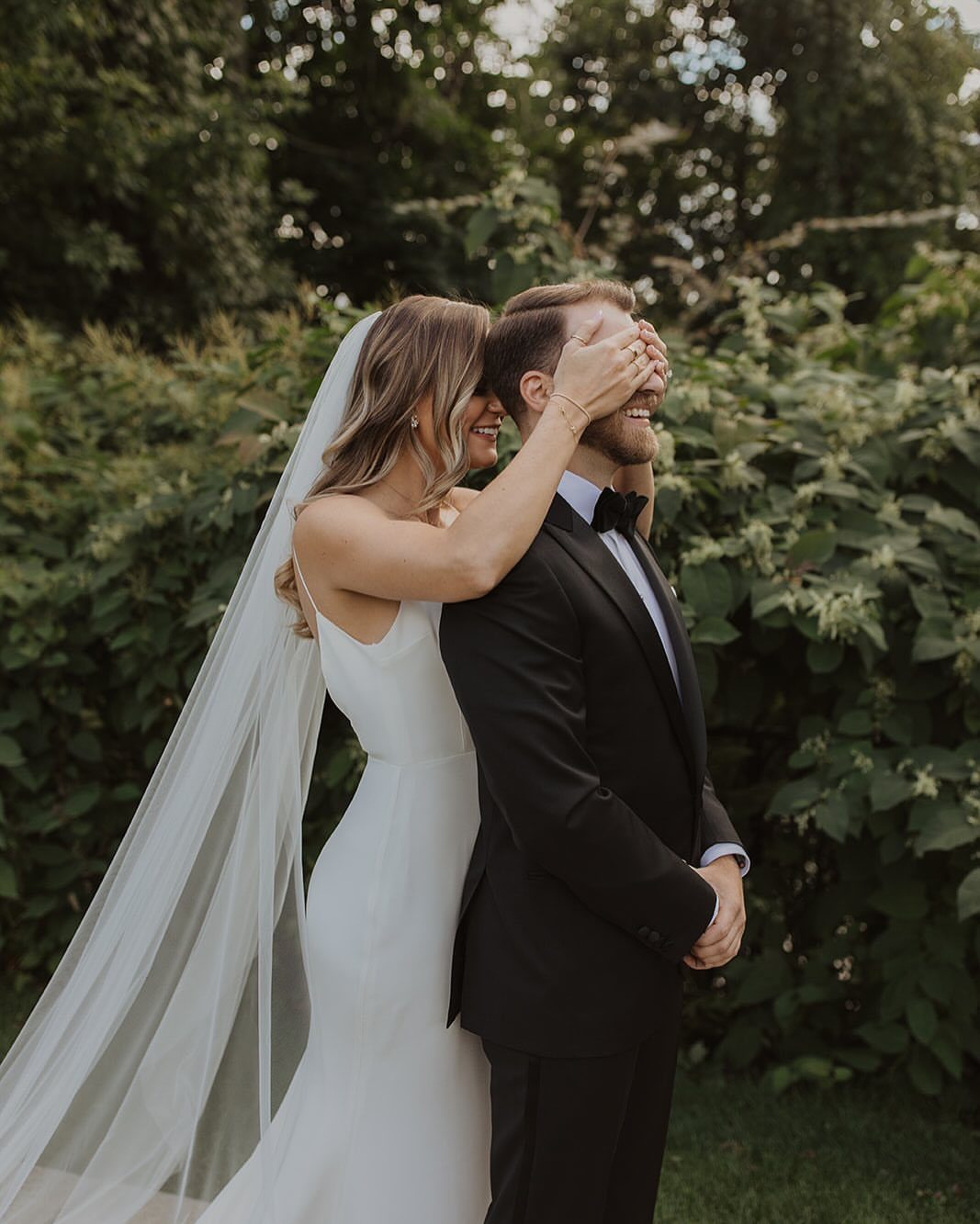 17 Couple Pictures for Your Wedding That Feel Real, Not Posed 1 A bride covering the groom's eyes with her hands during a first look outdoors.