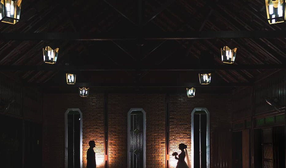 17 Couple Pictures for Your Wedding That Feel Real, Not Posed 17 Silhouetted bride and groom standing against warm light in a dark, rustic brick room.