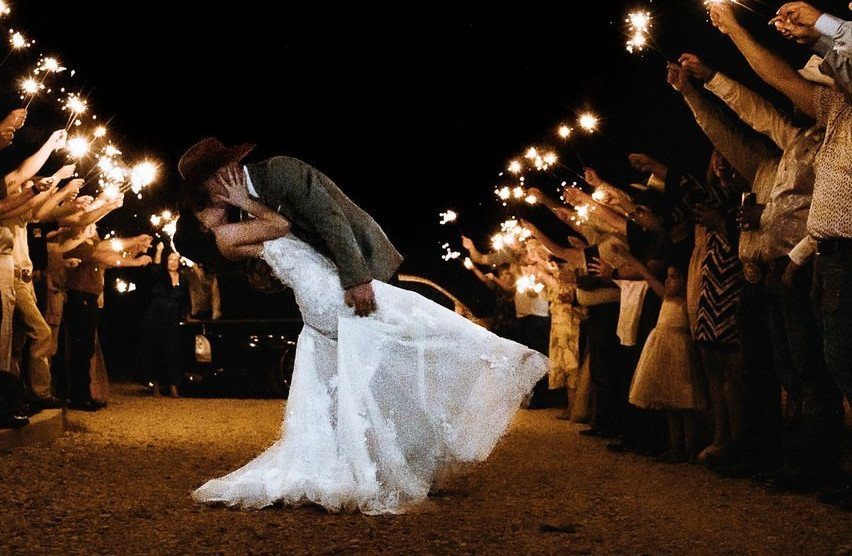17 Couple Pictures for Your Wedding That Feel Real, Not Posed 14 A bride and groom kissing during a dip pose surrounded by guests with sparklers.