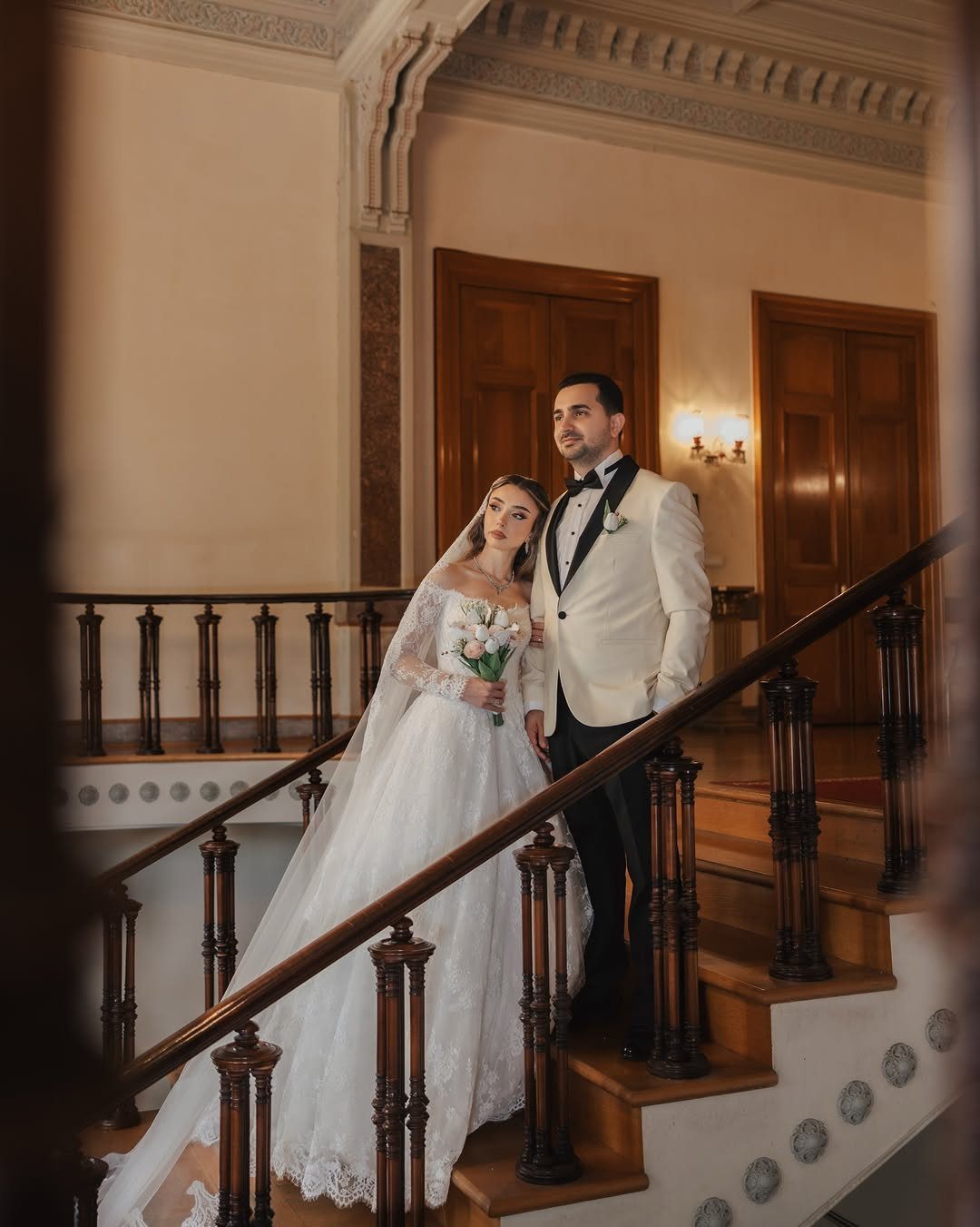 17 Couple Pictures for Your Wedding That Feel Real, Not Posed 4 A bride and groom posing together on an elegant indoor wooden staircase.