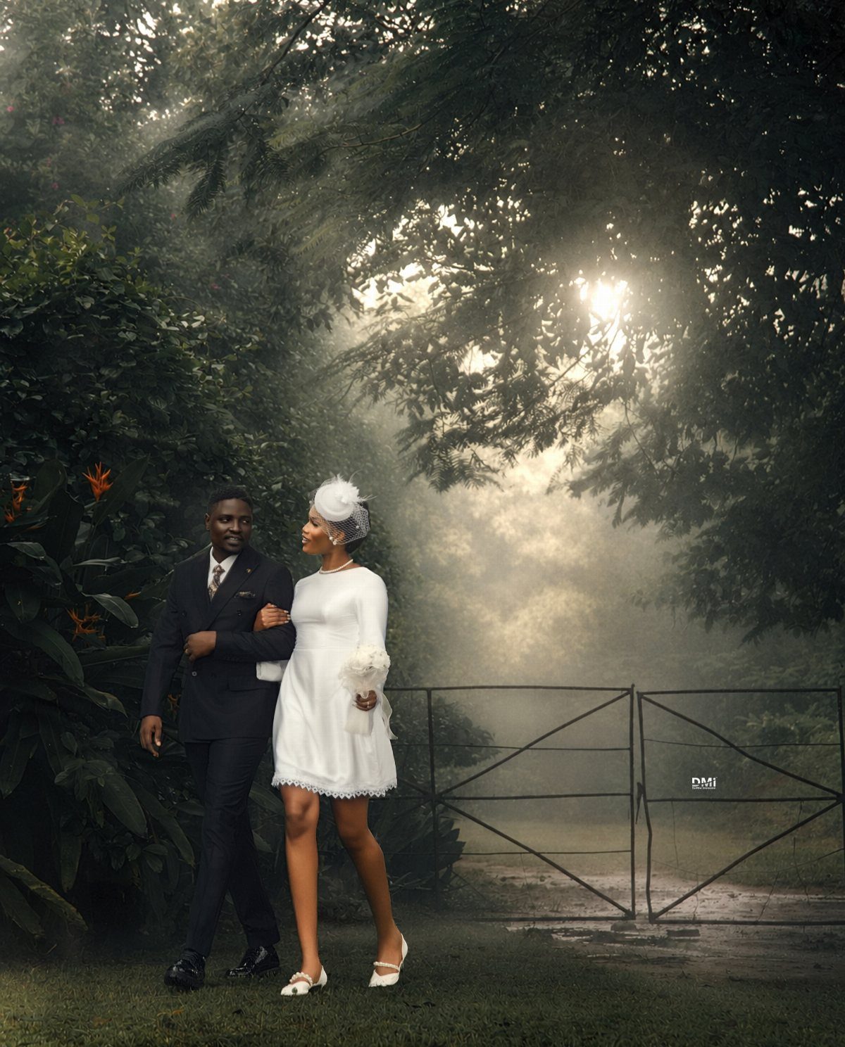 17 Couple Pictures for Your Wedding That Feel Real, Not Posed 2 A couple in formal attire walking through a misty, sunlit forest near a gate.