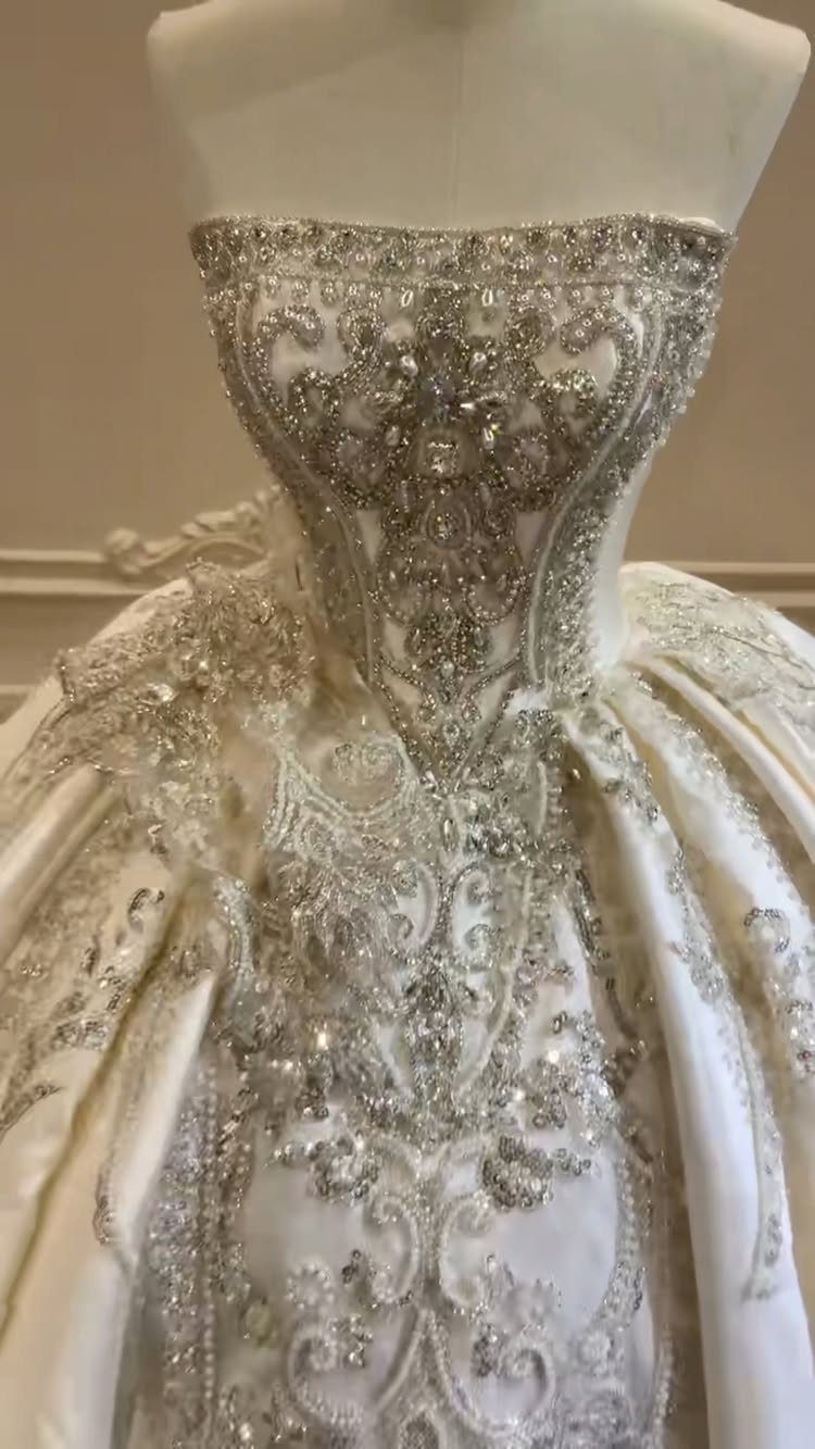 An ornate white wedding gown with heavy silver crystal and sequin embellishments on a mannequin.
