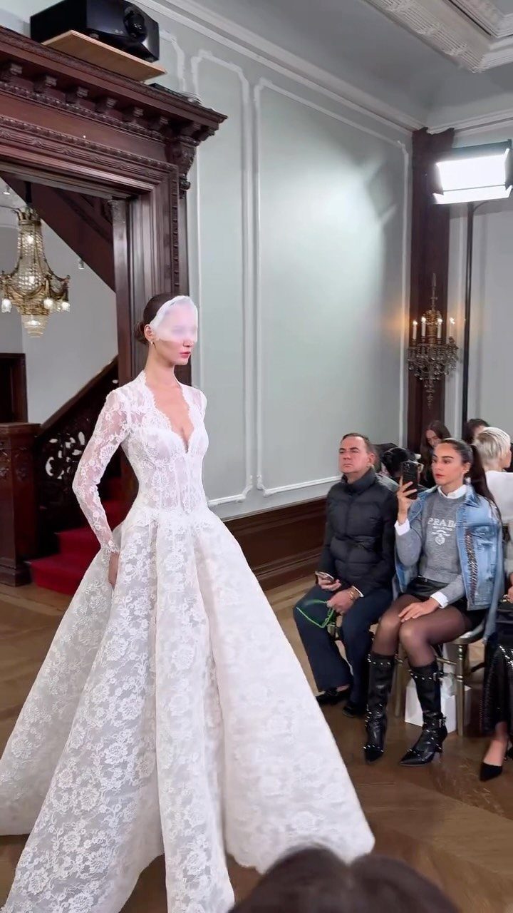 Model walking in a white lace wedding gown with long sleeves and a full skirt.