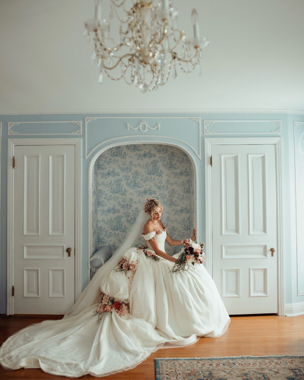 A bride wearing a voluminous white wedding gown poses in a light blue room.