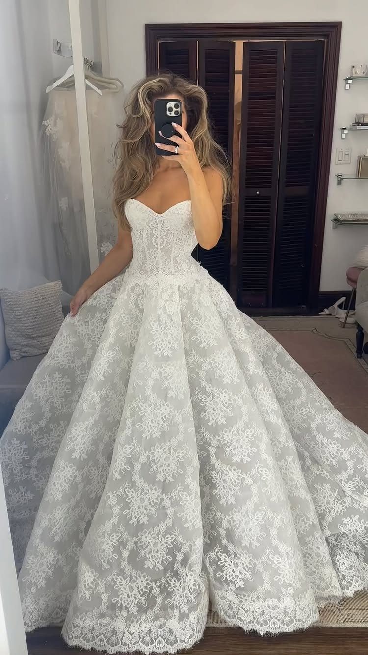 Woman in a white lace strapless ballgown wedding dress taking a mirror selfie.