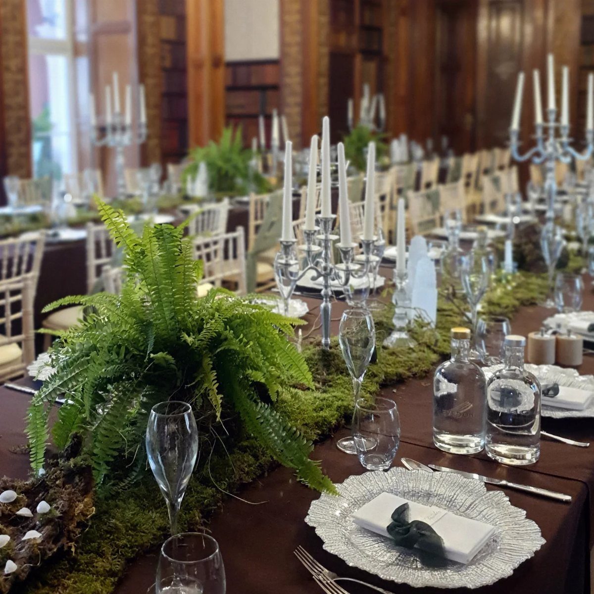 11 Forest Theme Wedding Ideas for a Natural Woodland Ceremony 8 Green ferns and moss runners decorate a long wedding reception table with silver candelabras and glassware.