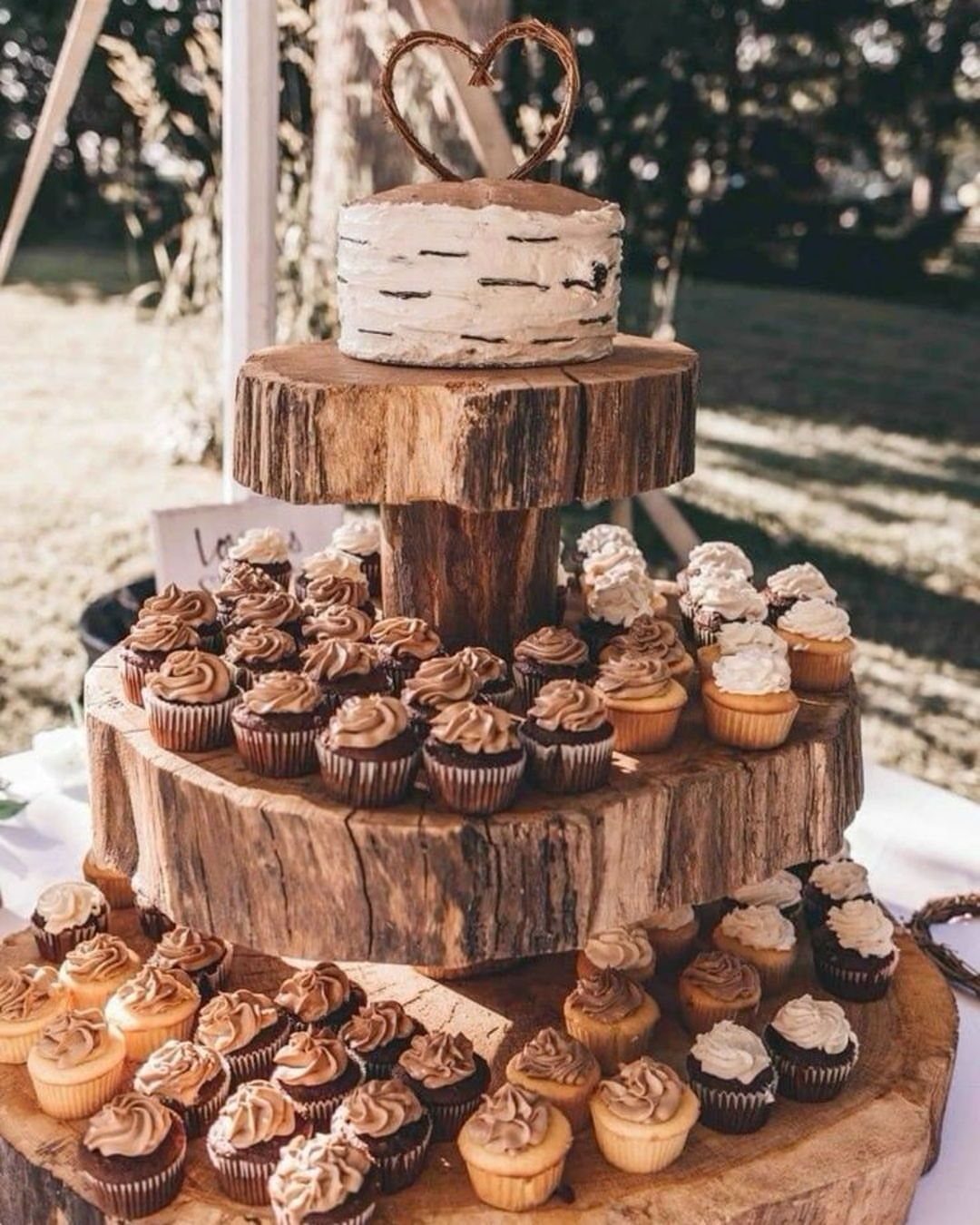 11 Forest Theme Wedding Ideas for a Natural Woodland Ceremony 11 Tiered rustic wooden tree slice cake stands displaying a birch cake and many cupcakes outdoors.