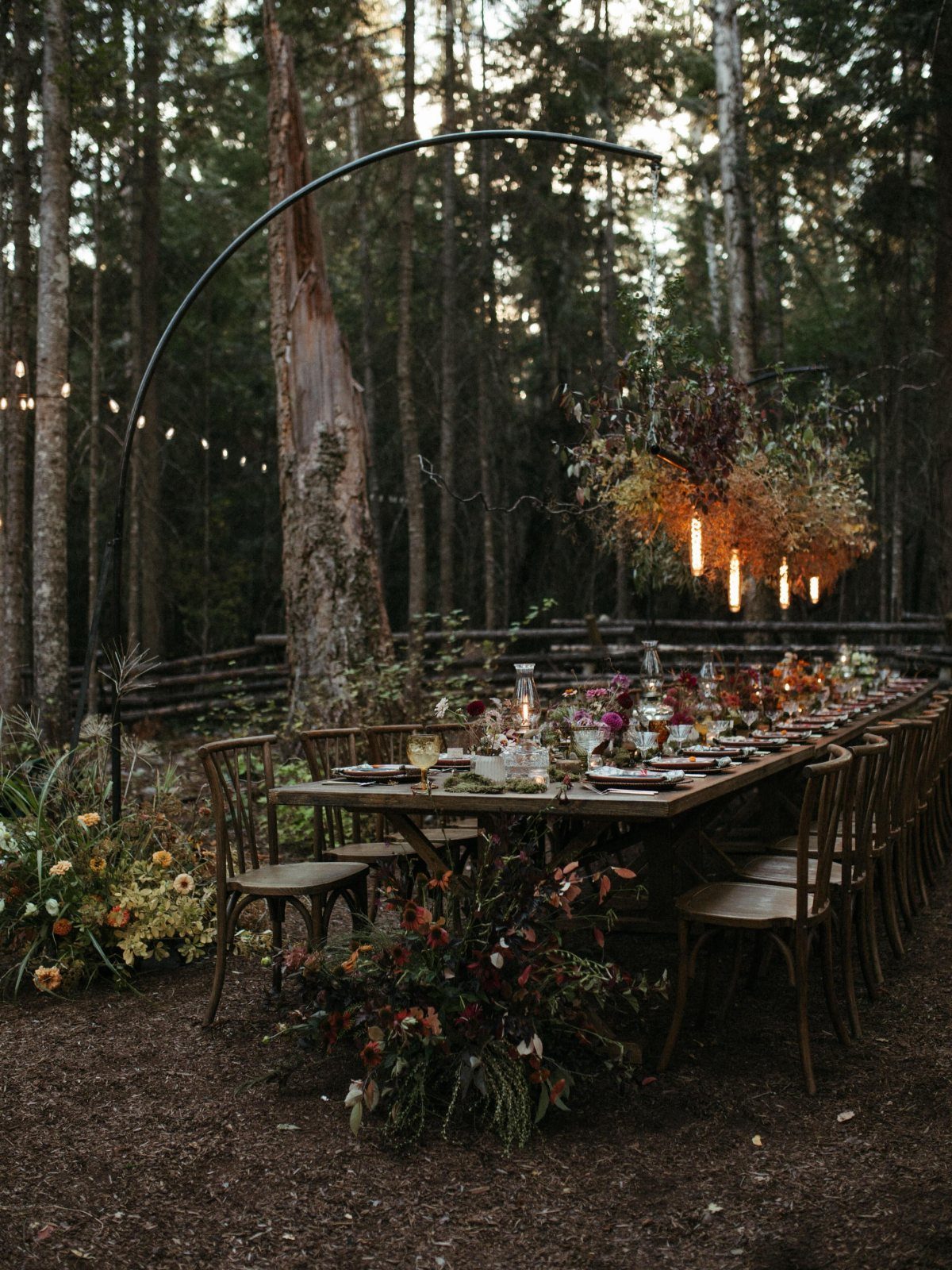 11 Forest Theme Wedding Ideas for a Natural Woodland Ceremony 5 A long rustic wooden dining table set with flowers and glassware in a forest setting.
