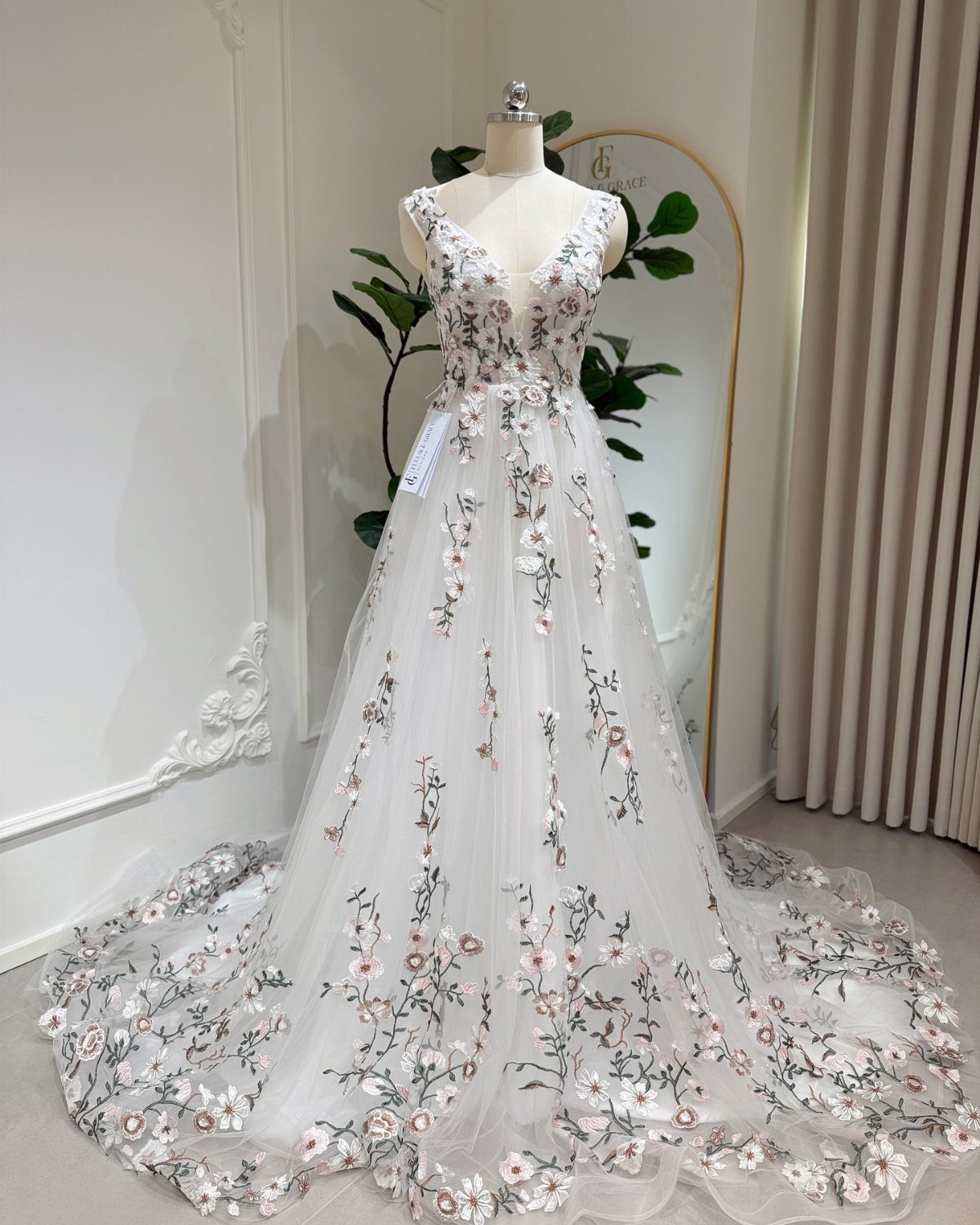 A white wedding gown with pink floral embroidery displayed on a mannequin.