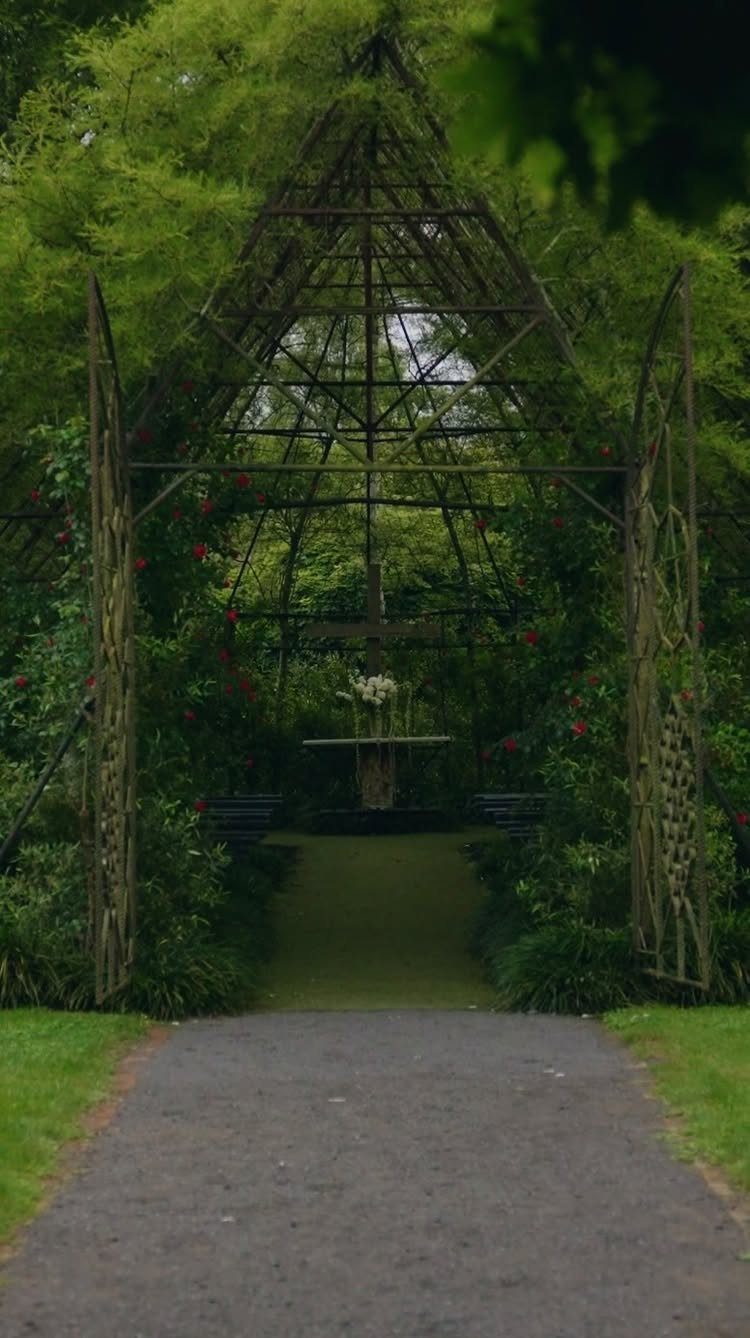 A large metal garden trellis structure surrounded by lush green trees and flowering bushes.