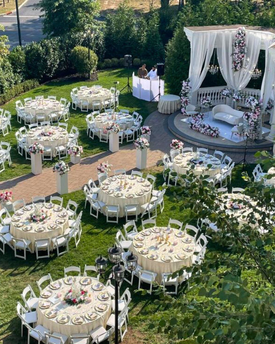 Round wedding tables with white linens and floral centerpieces arranged on a green lawn.