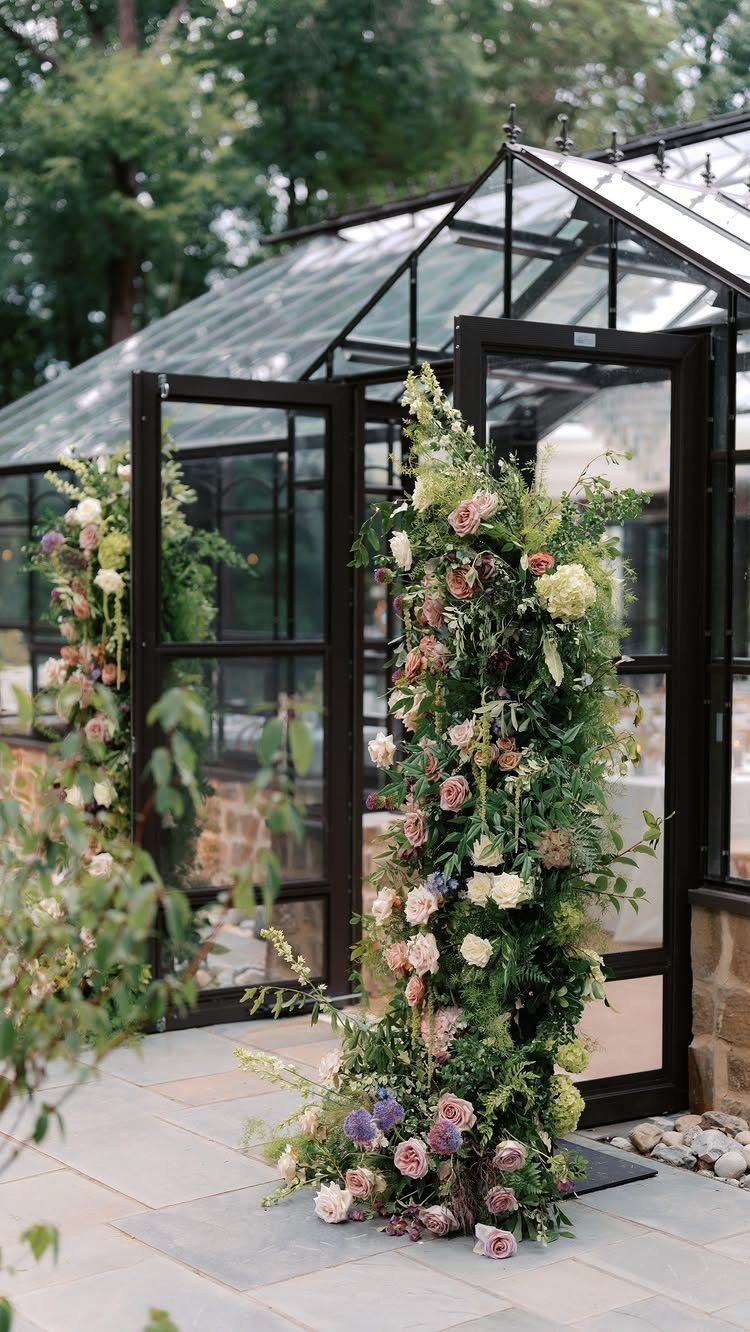 Garden Wedding Ceremony: 9 Ideas for Intimate Outdoor Vows 9 Floral arrangements decorate the entrance of a large glass greenhouse on a stone patio.
