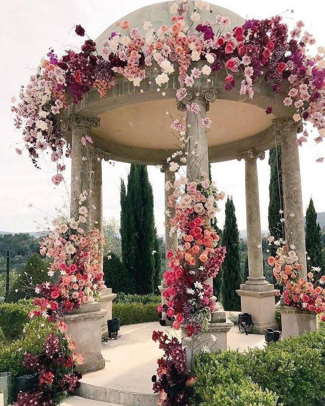 Garden Wedding Ceremony: 9 Ideas for Intimate Outdoor Vows 3 A stone gazebo adorned with vibrant pink and white floral arrangements in a lush garden.