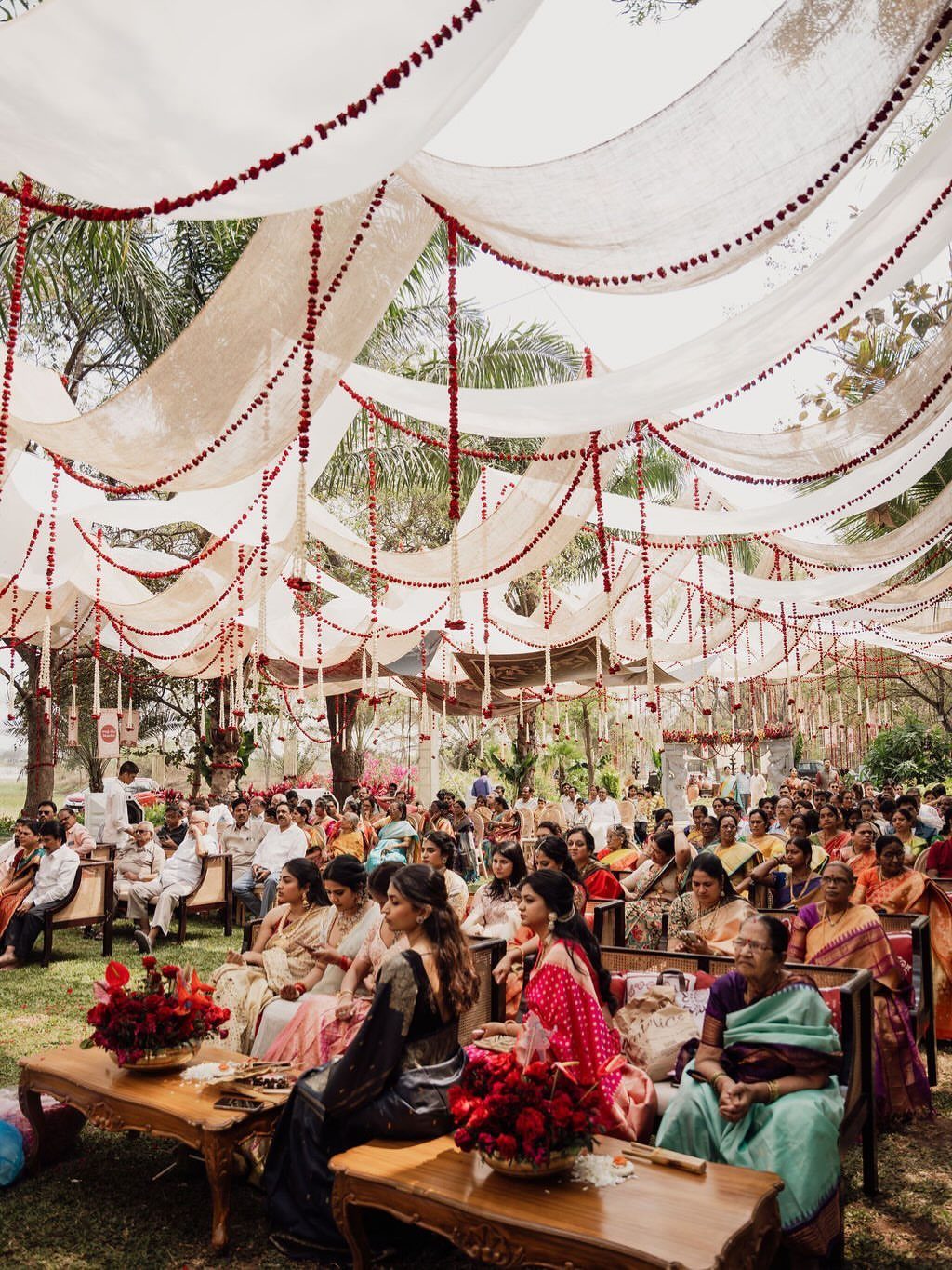 Garden Wedding Ceremony: 9 Ideas for Intimate Outdoor Vows 2 Guests seated on wooden benches under a white fabric canopy decorated with red flower garlands.