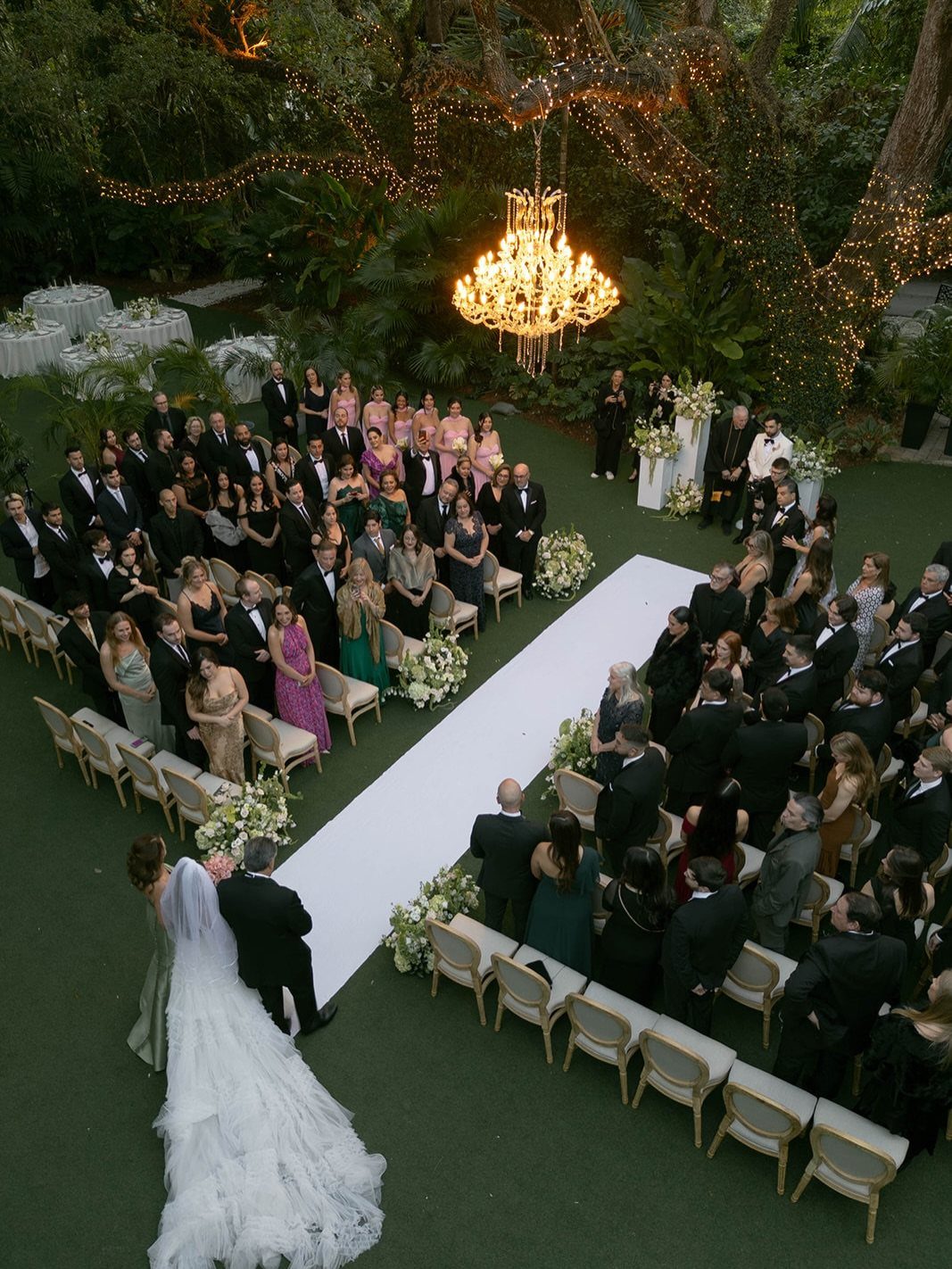 Garden Wedding Ceremony: 9 Ideas for Intimate Outdoor Vows 6 A bride in a white gown walks down a white aisle during an outdoor garden wedding ceremony.