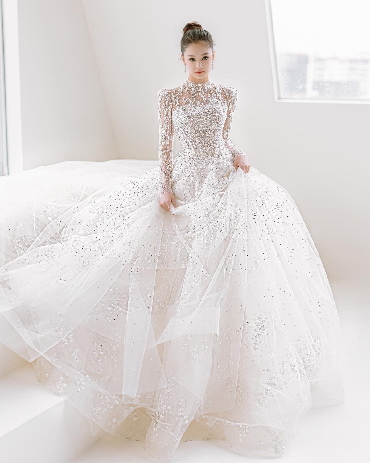 Glam Wedding Dress: 5 Looks for 2026 4 Woman in a sparkling, long-sleeved embellished wedding gown with a voluminous tulle skirt.