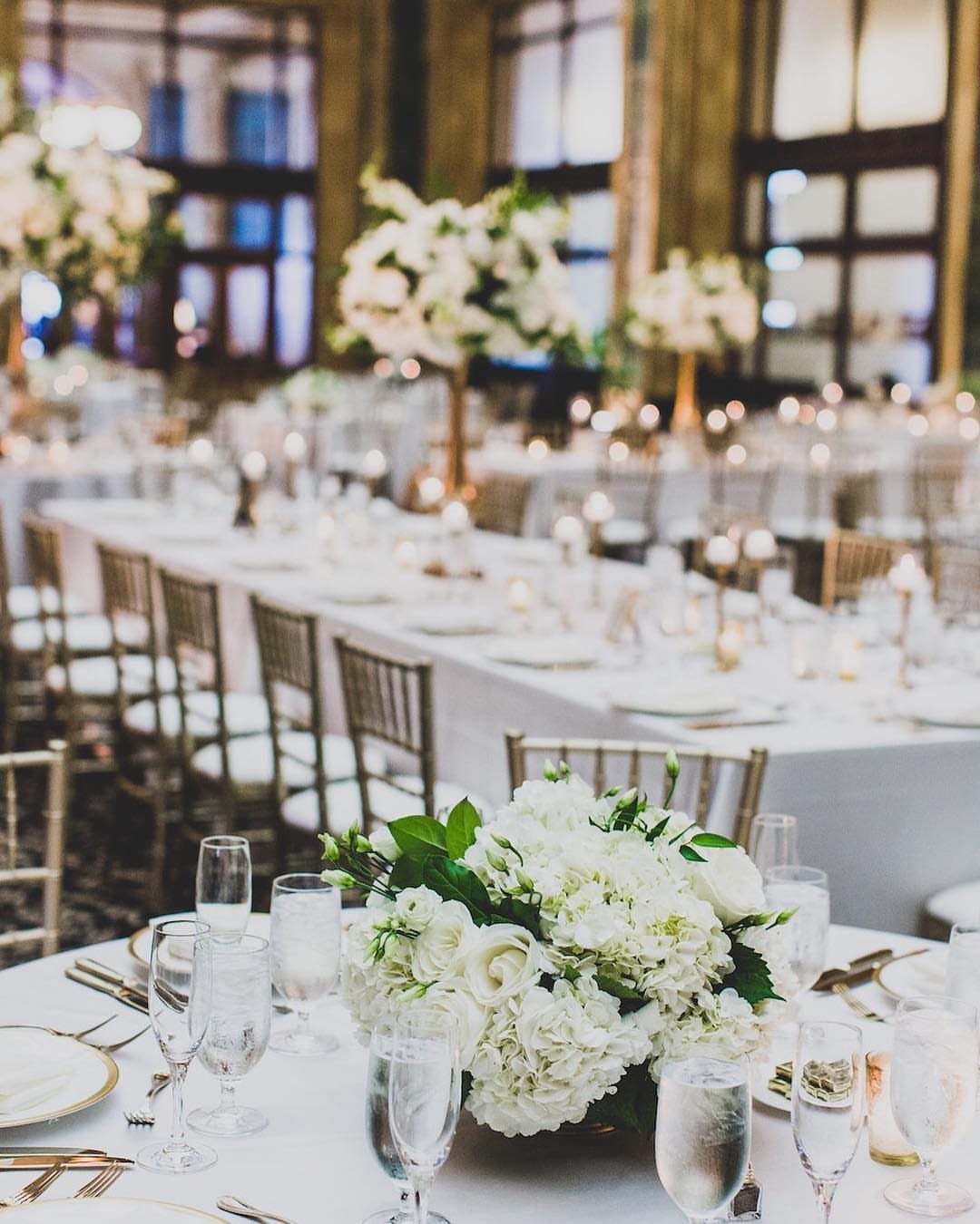 Gold and Champagne Wedding: 7 Ideas for a Warm, Metallic Celebration 4 White floral centerpieces and linens on long banquet tables in an elegant wedding reception hall.